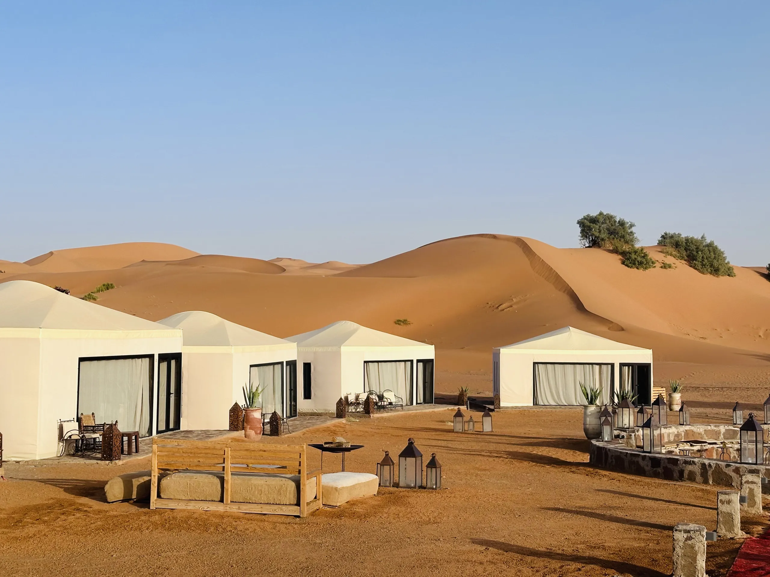 Luxury desert camp with modern white tents set against golden sand dunes and clear blue sky - morocco.